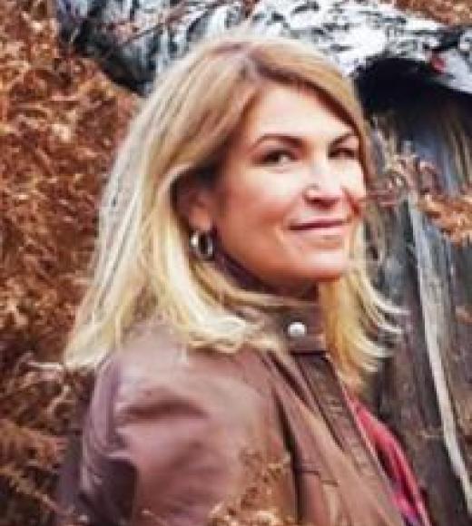 A photo of a woman wearing a brown coat near autumnal leaves