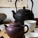 Black cast-iron kettle, purple clay teapot and white porcelain cups on wooden table